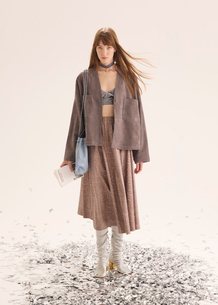 Woman in a brown outfit with a blue bag standing on a textured surface.