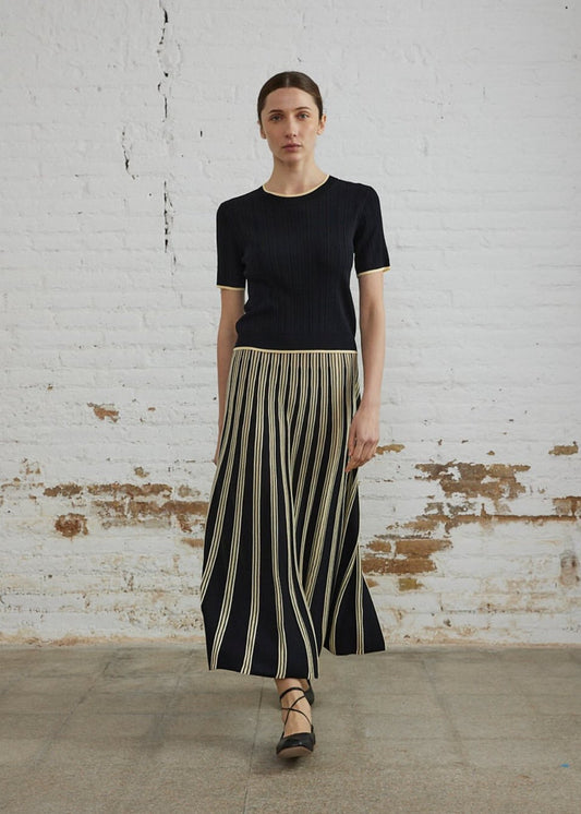 Woman wearing a black top and striped skirt against a white brick wall.