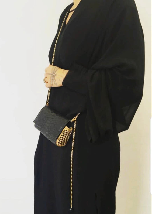 Black outfit with gold chain detail on a plain background