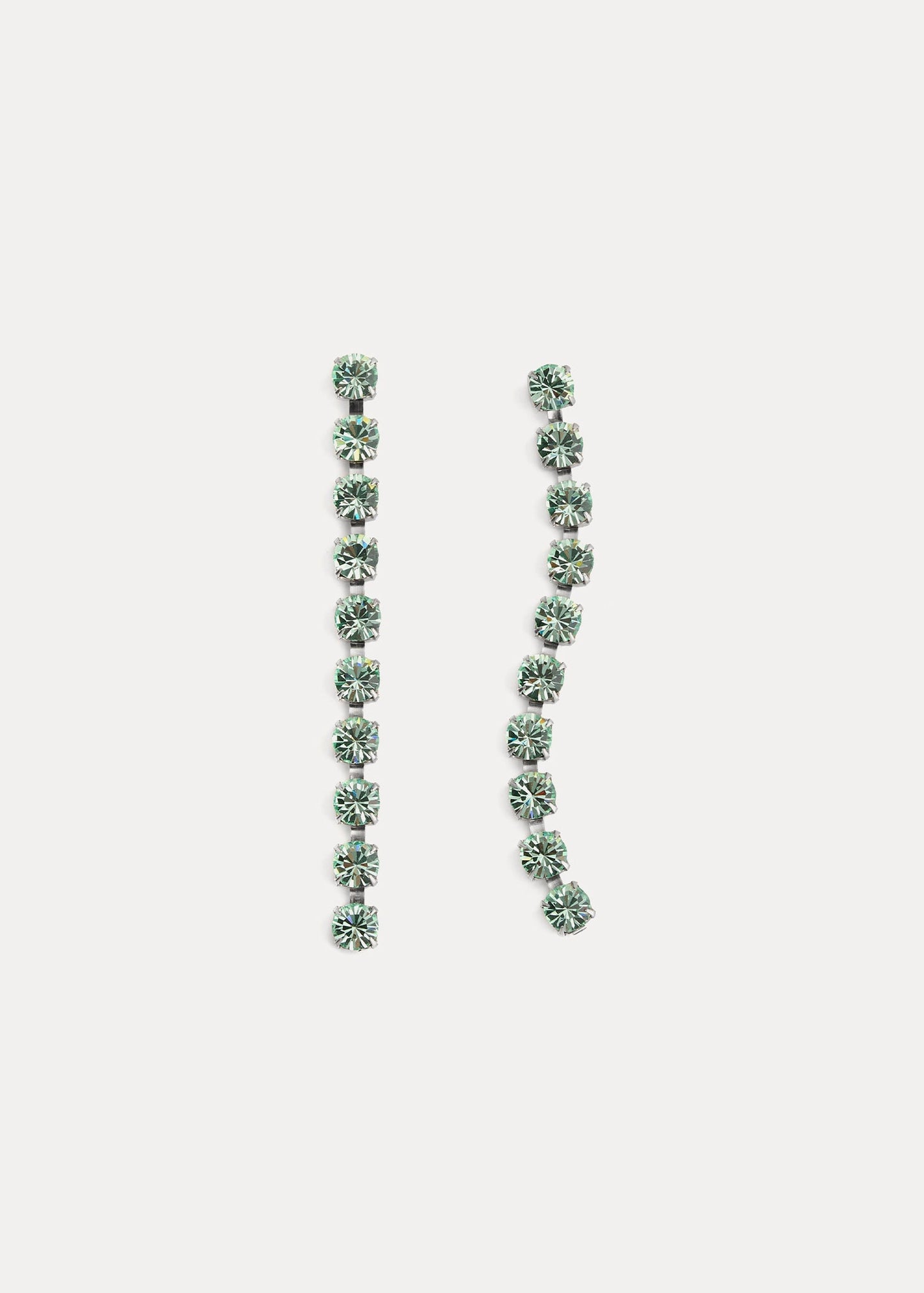 Pair of long, thin earrings with green gemstones on a light gray background