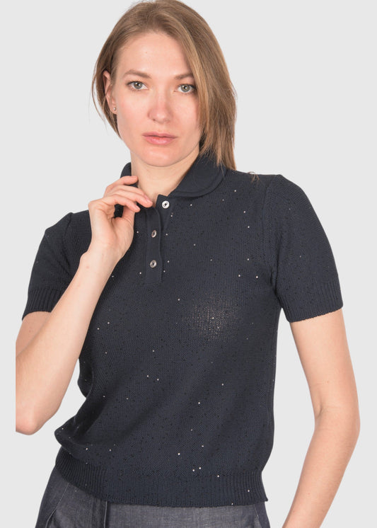 A woman modeling a short-sleeve knit polo shirt in a very dark navy or near-black color with small scattered light reflective dot details, against a plain light gray studio background.