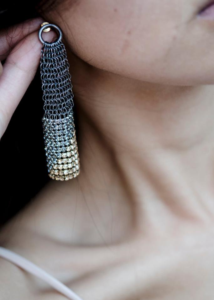 A close-up of a person wearing silver and gold diagonal earrings with a geometric pattern.