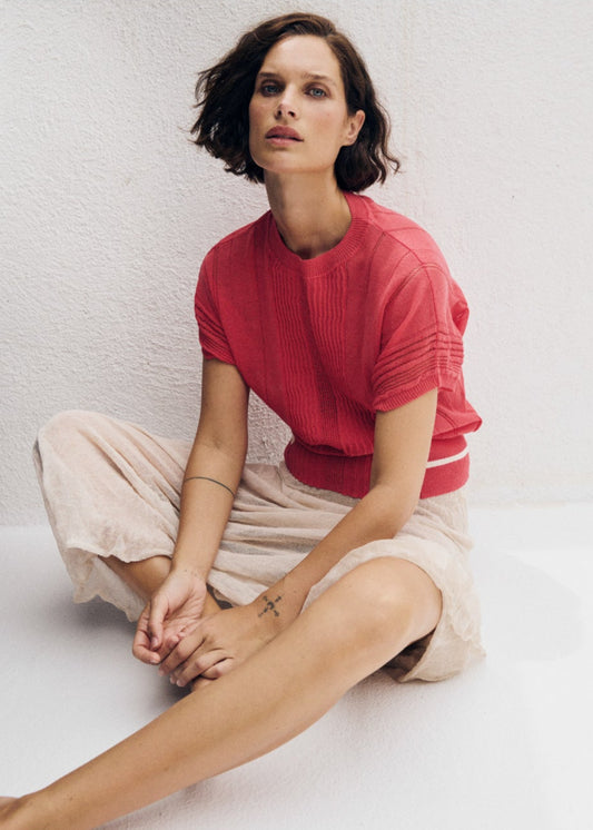 Woman sitting on a white floor wearing a red sweater and beige pants, with text overlay.