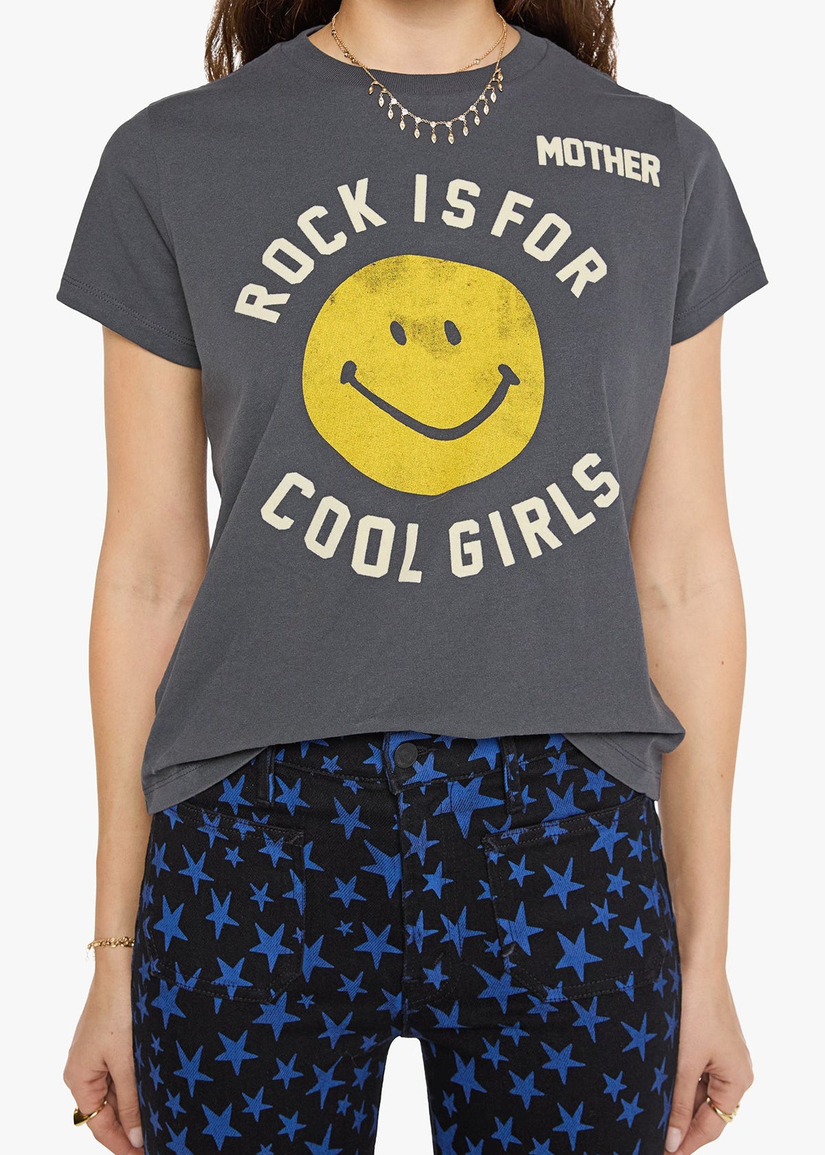 A woman wearing a dark gray graphic t-shirt with a yellow smiley face and the text 'ROCK IS FOR COOL GIRLS' and 'MOTHER', paired with blue star-patterned leggings.