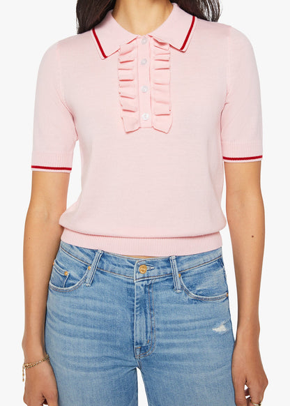A woman wearing a light pink short-sleeve knit polo shirt with red piping trim on the collar, sleeve cuffs, and a ruffled placket detail, paired with blue jeans.