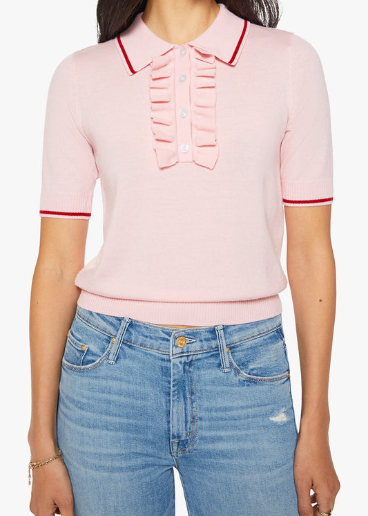 A woman wearing a light pink short-sleeve knit polo shirt with red piping trim on the collar, sleeve cuffs, and a ruffled placket detail, paired with blue jeans.
