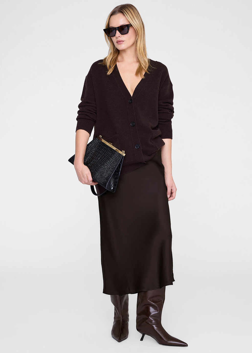 Woman wearing a dark brown cardigan, dress, and boots on a white background