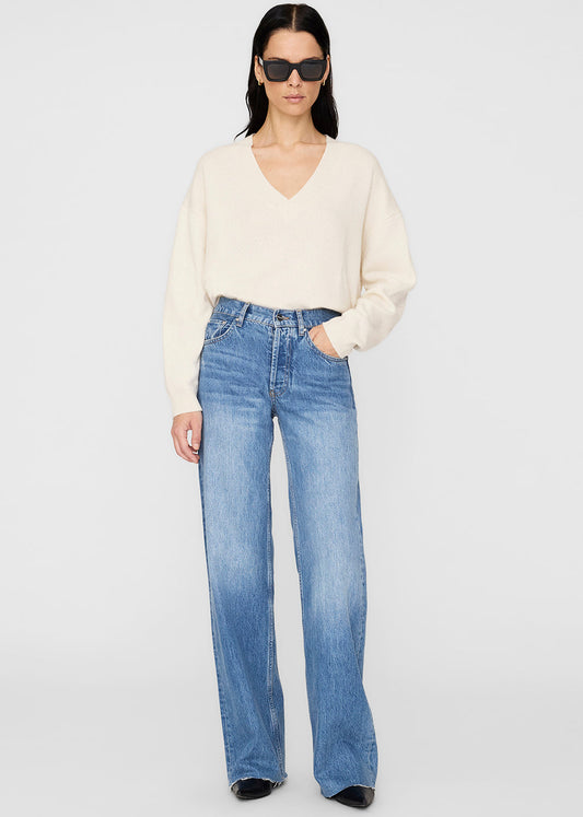 Woman wearing a cream sweater and blue jeans on a white background