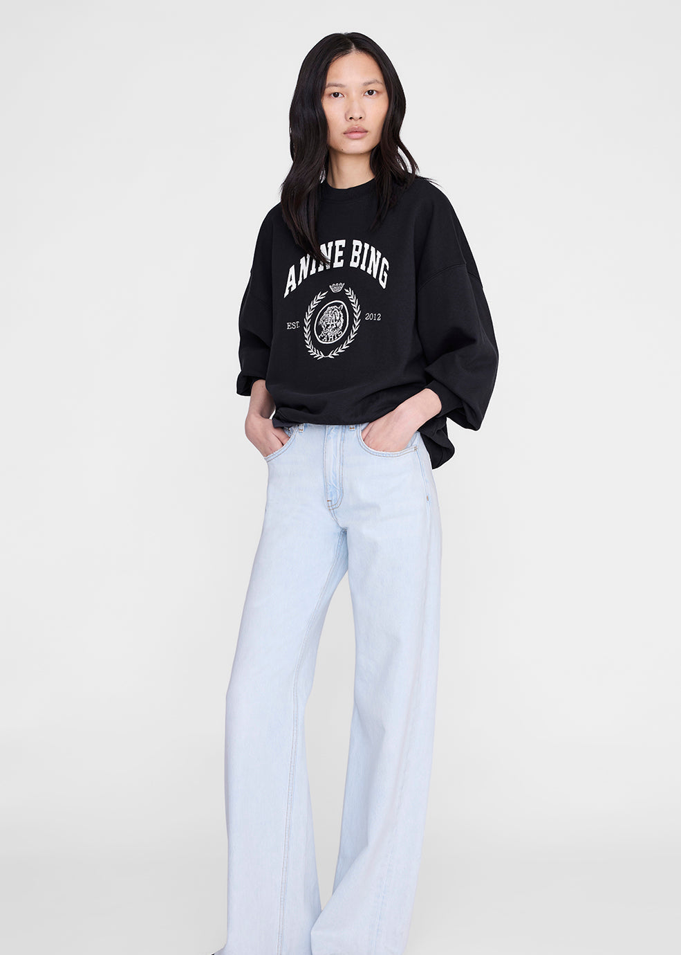 Person wearing a black sweatshirt with white text and light blue jeans on a white background