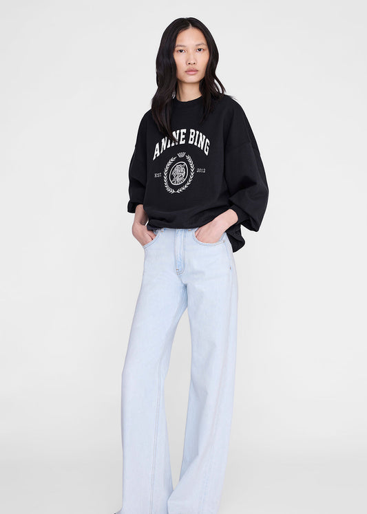 Person wearing a black sweatshirt with white text and light blue jeans on a white background