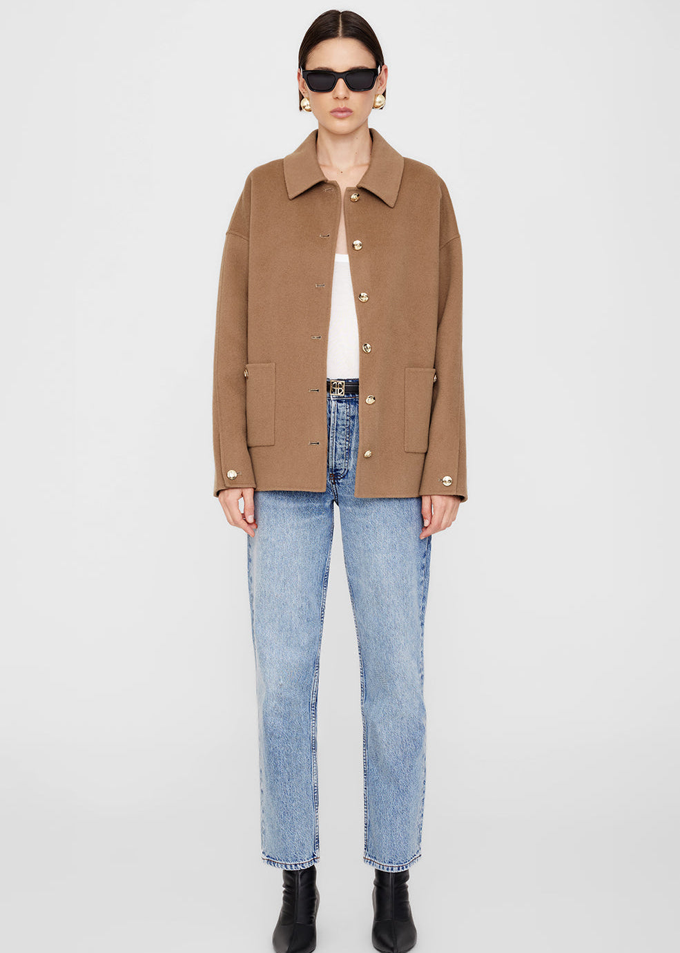 Person wearing a brown jacket, white shirt, blue jeans, and black shoes on a white background