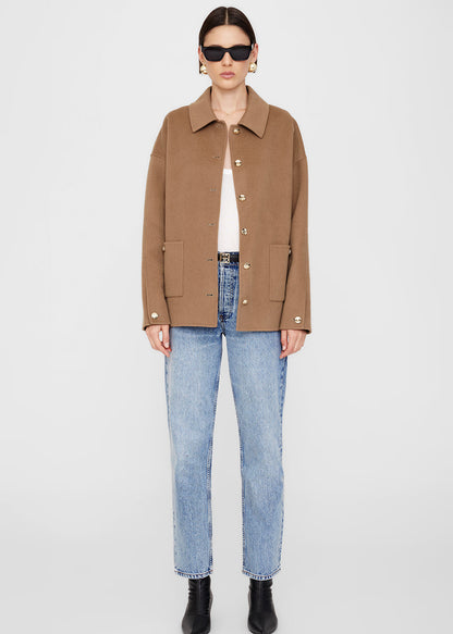 Person wearing a brown jacket, white shirt, blue jeans, and black shoes on a white background