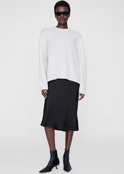 Person wearing a white sweater, black skirt, and black boots on a white background