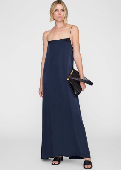 Woman wearing a navy blue slip dress holding a black clutch against a white background