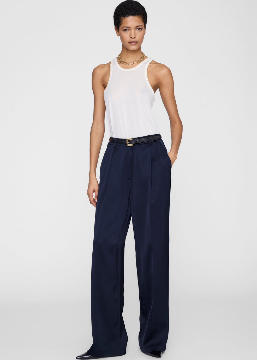 Woman wearing a white sleeveless top and navy wide-leg pants on a white background