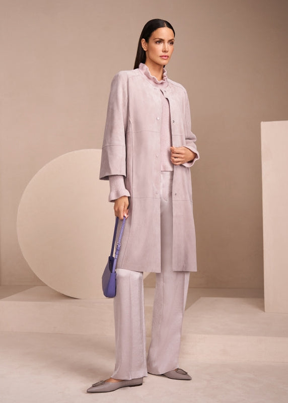 Woman in a light gray outfit holding a blue bag against a neutral background