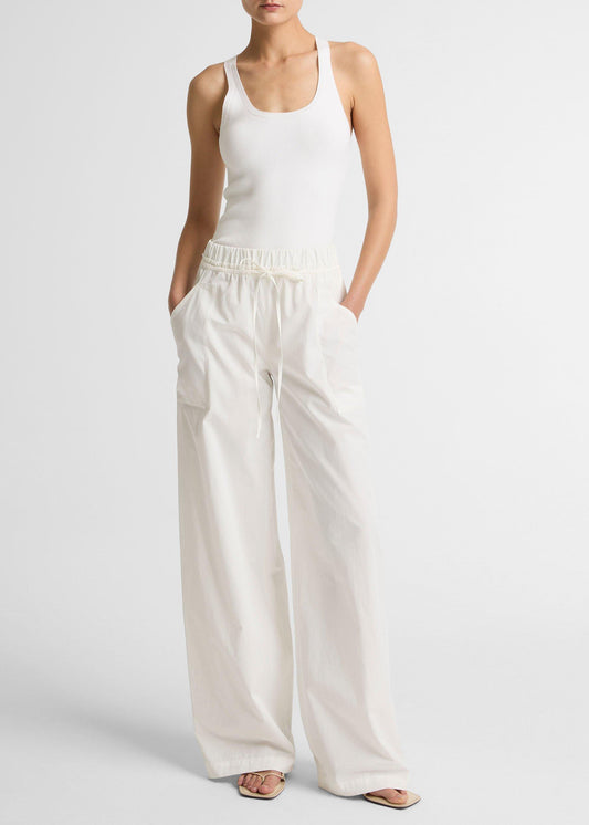 Person wearing a white tank top and wide-leg pants on a plain background