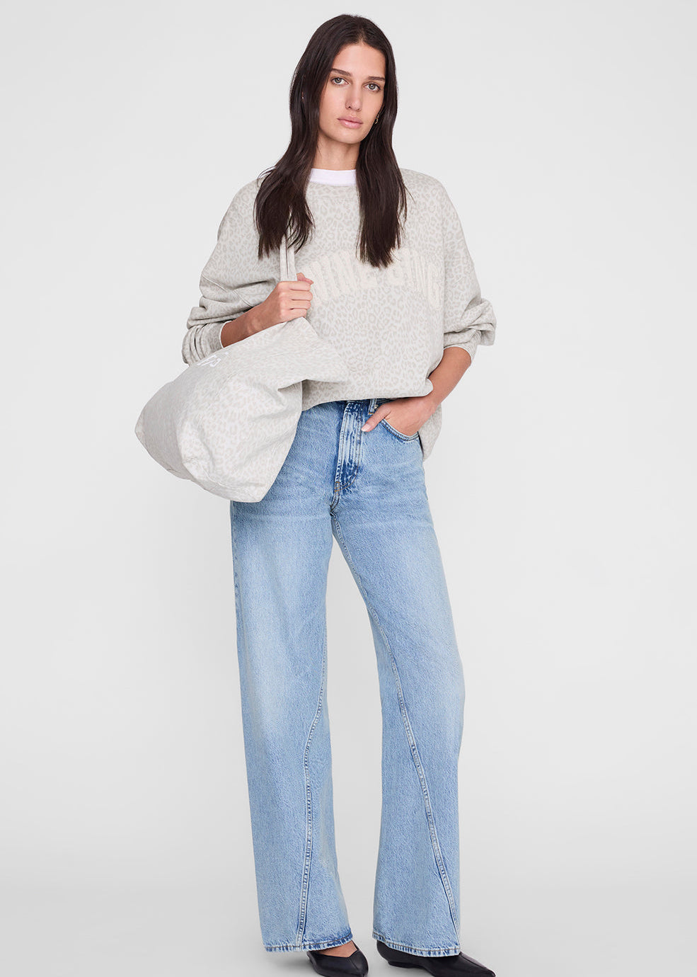 Woman wearing a light gray sweater and blue jeans on a white background