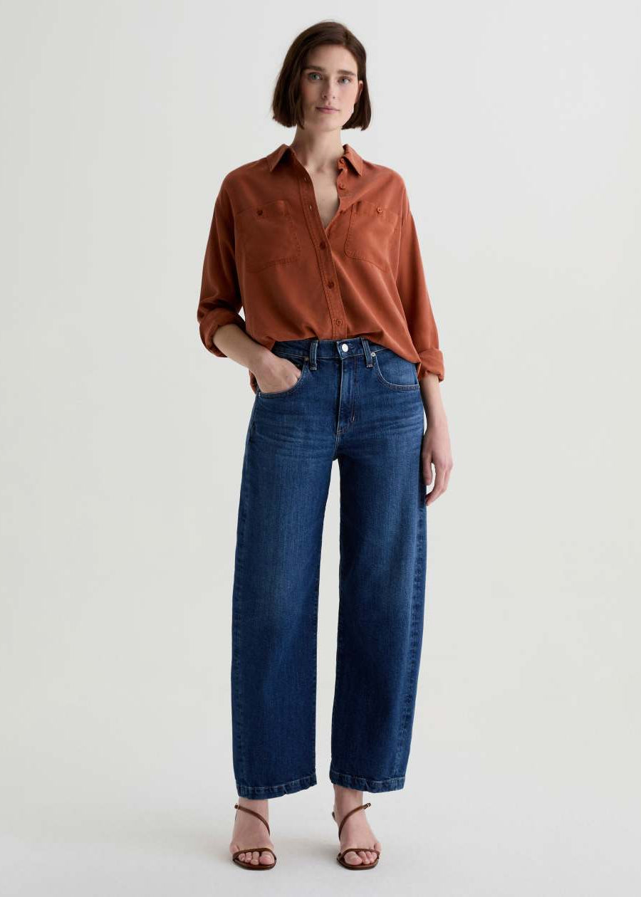 Woman wearing a rust-colored shirt and blue jeans on a white background