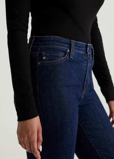 Person wearing dark blue jeans and a black long-sleeve top on a light background