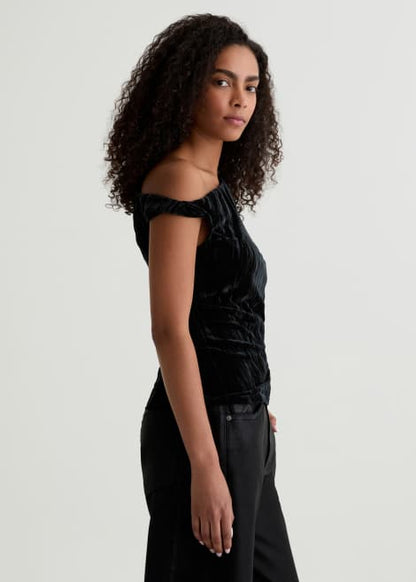 Woman wearing a black off-shoulder top and black pants against a plain background