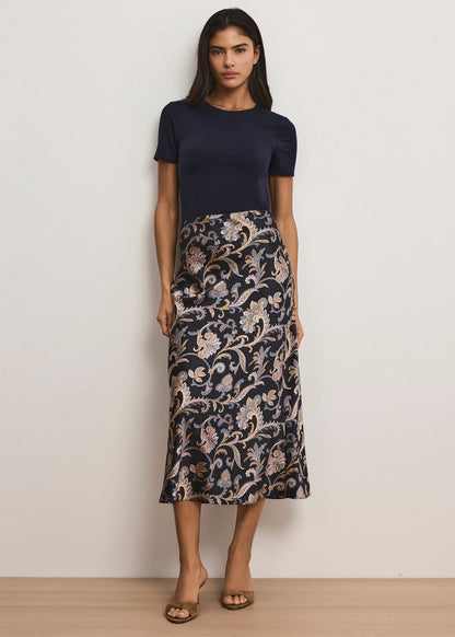 Woman wearing a navy top and patterned skirt against a plain background