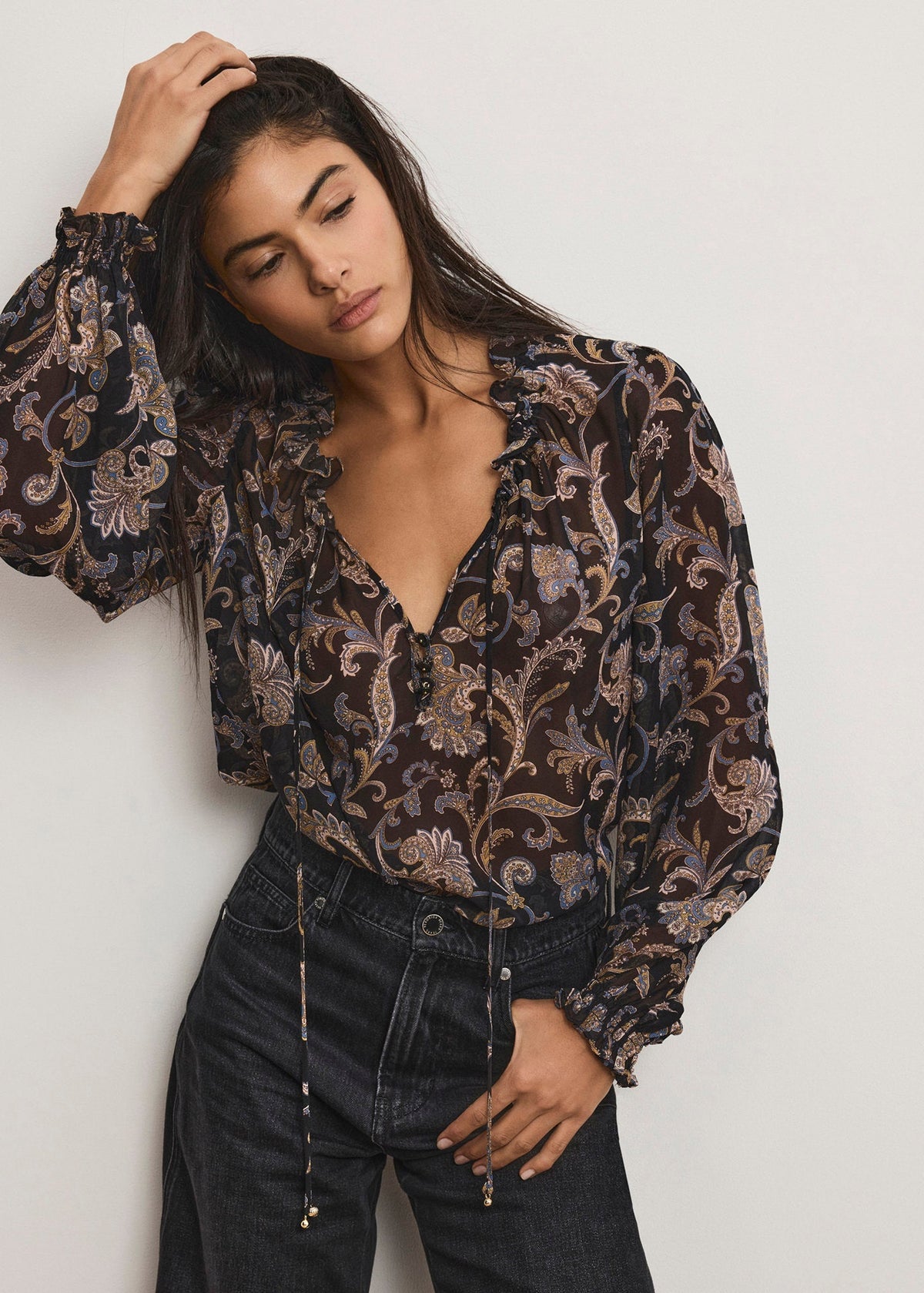 Woman wearing a patterned blouse and black pants against a plain background