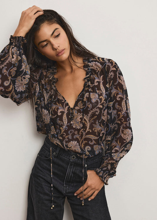 Woman wearing a patterned blouse and black pants against a plain background