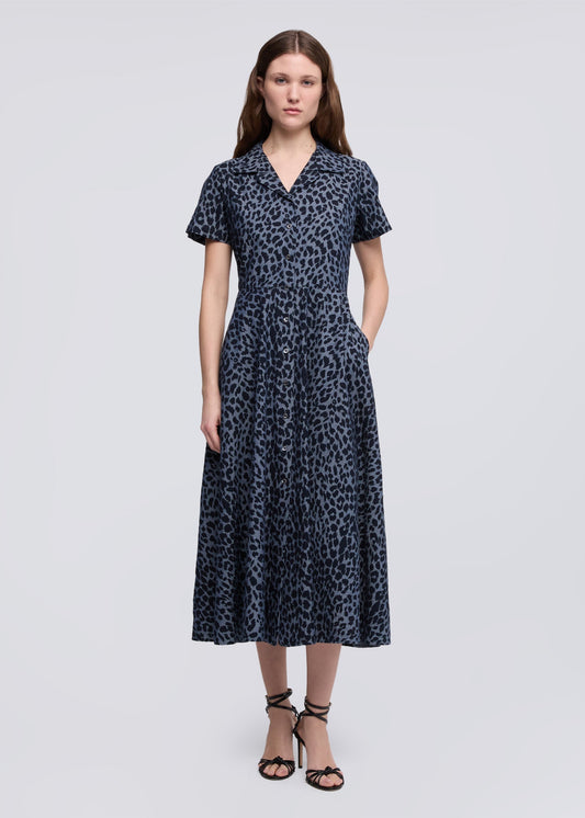 A woman modeling a short-sleeve midi dress with a dark navy blue and black leopard print pattern, paired with black strappy high-heeled sandals, against a light gray studio background.