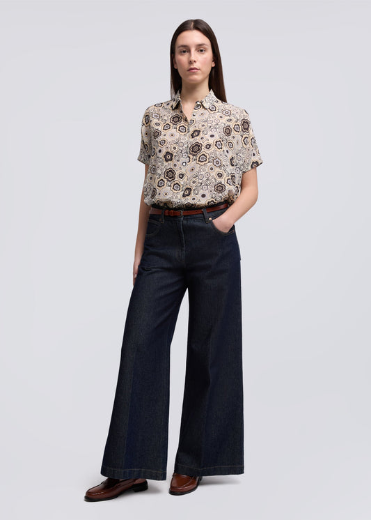 Woman wearing a patterned blouse and dark jeans on a light gray background