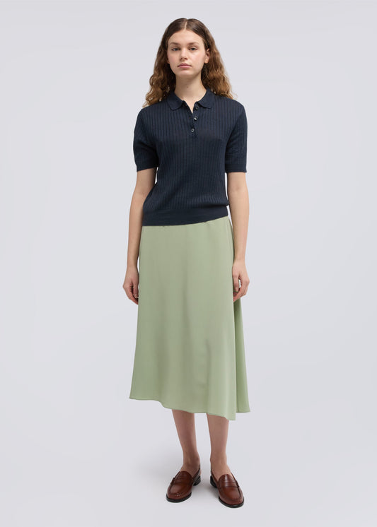 Woman wearing a dark blue polo shirt and light green skirt on a white background