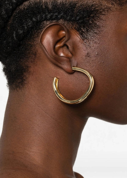 A close-up side profile of a model wearing a thick, polished gold hoop earring.