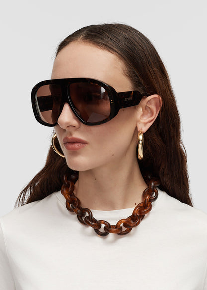 Woman wearing large sunglasses and a brown necklace on a white background