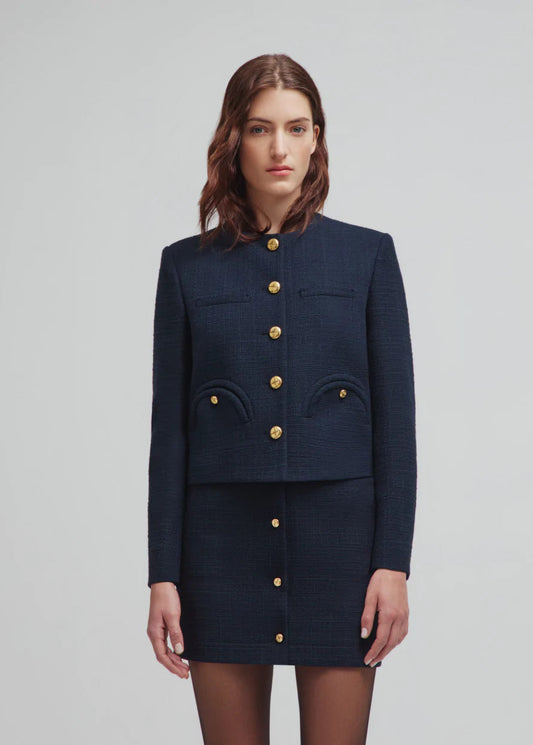 Woman wearing a navy blue outfit with gold buttons on a light gray background