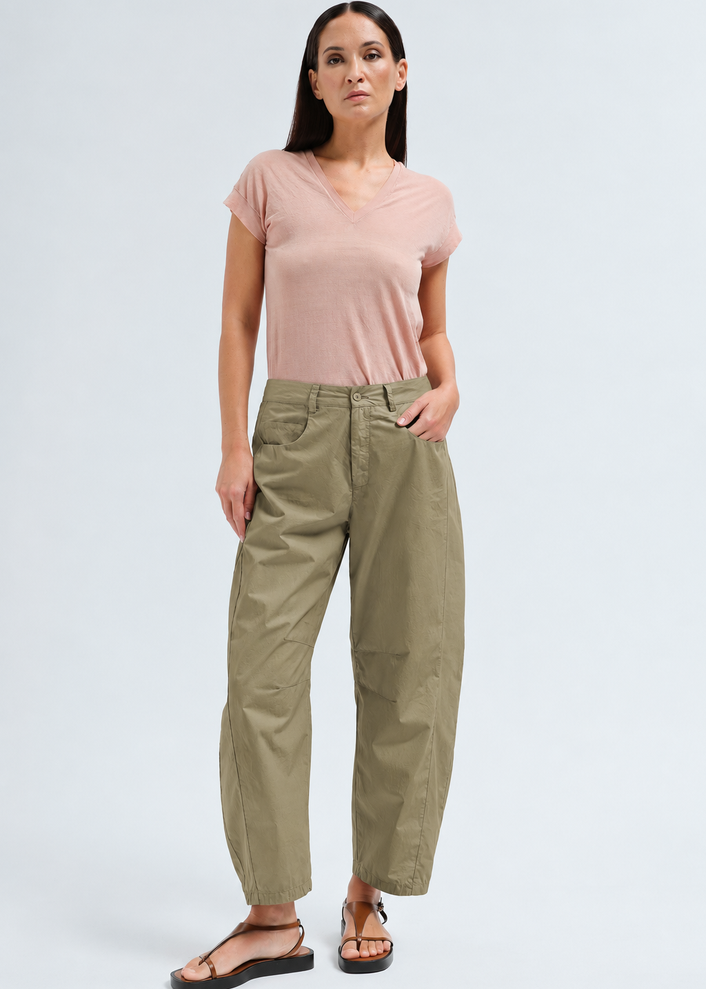 A woman modeling a light pink short-sleeve V-neck t-shirt and olive green wide-leg cropped pants with black sandals, standing against a light gray studio background.