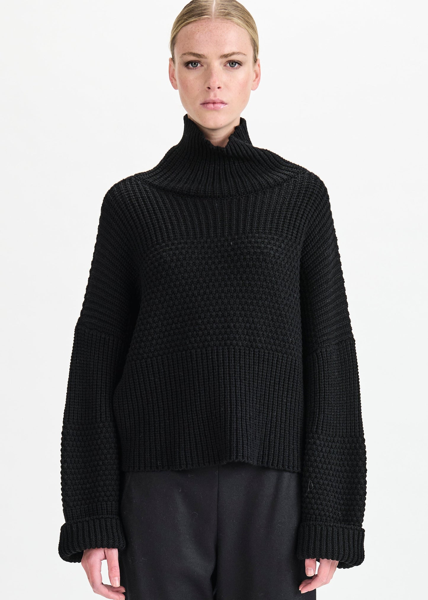 Person wearing a black ribbed sweater on a white background