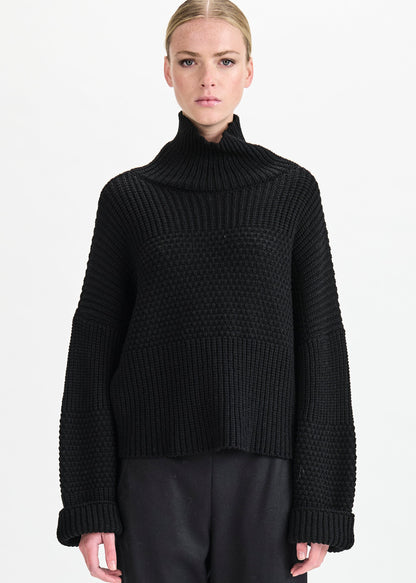 Person wearing a black ribbed sweater on a white background