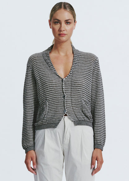 Woman wearing a gray patterned cardigan and white pants on a light gray background