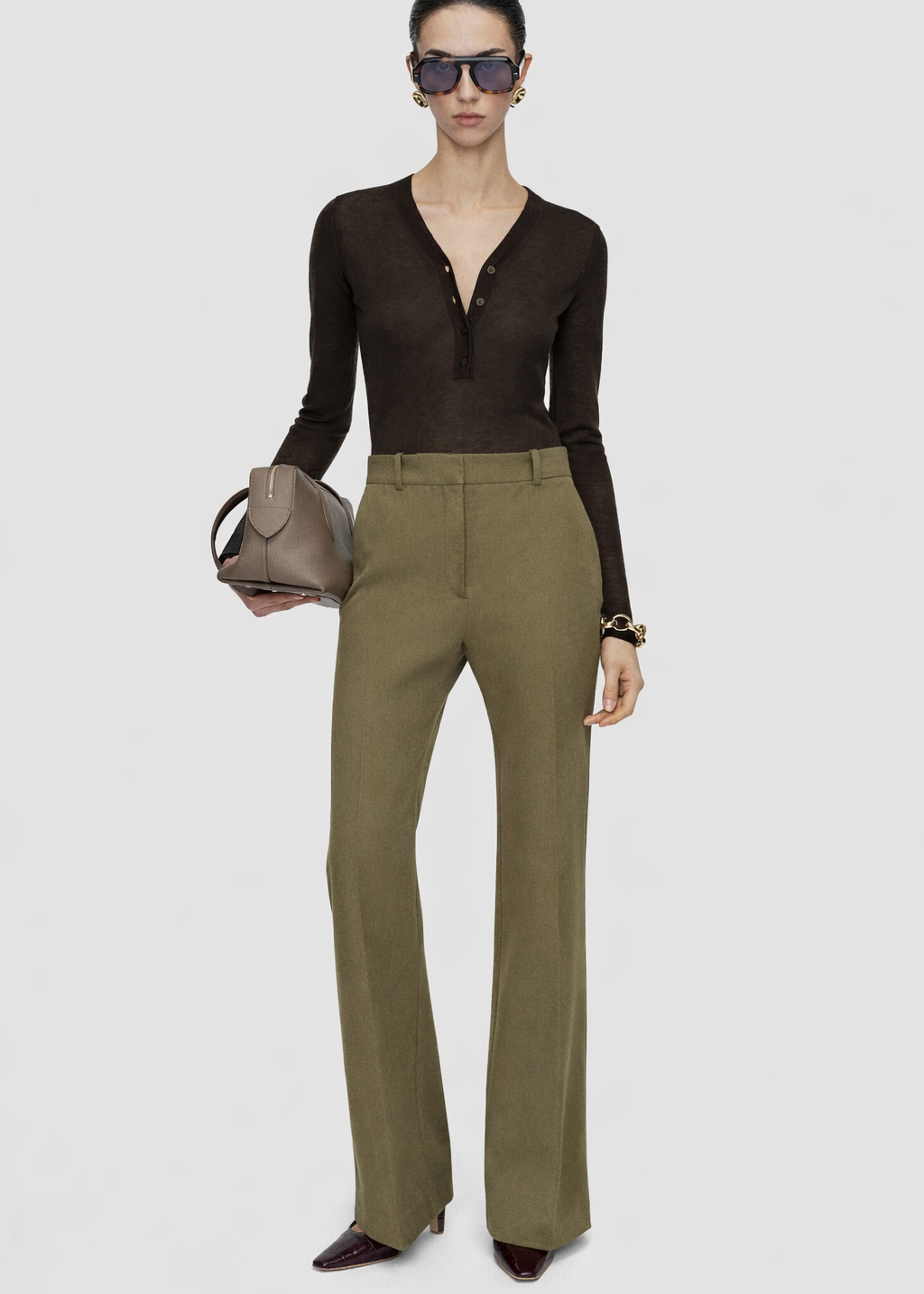 Woman wearing a brown top and green pants with a beige handbag on a white background