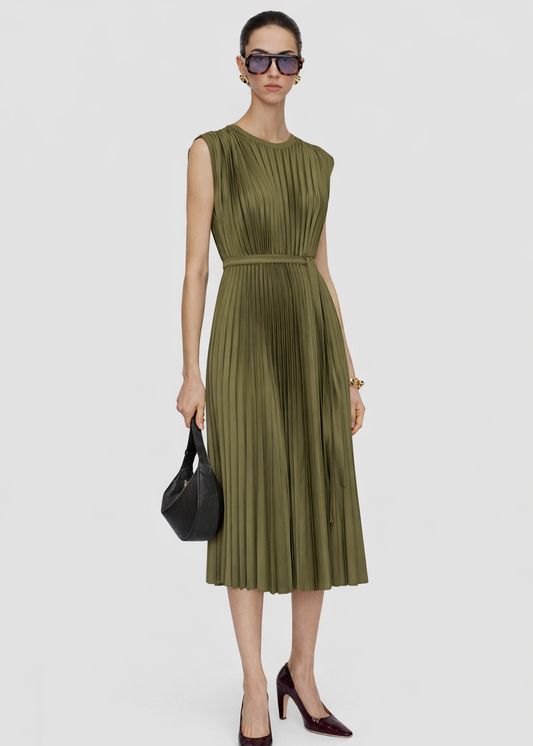 Woman wearing a green pleated dress with sunglasses and a black handbag on a white background