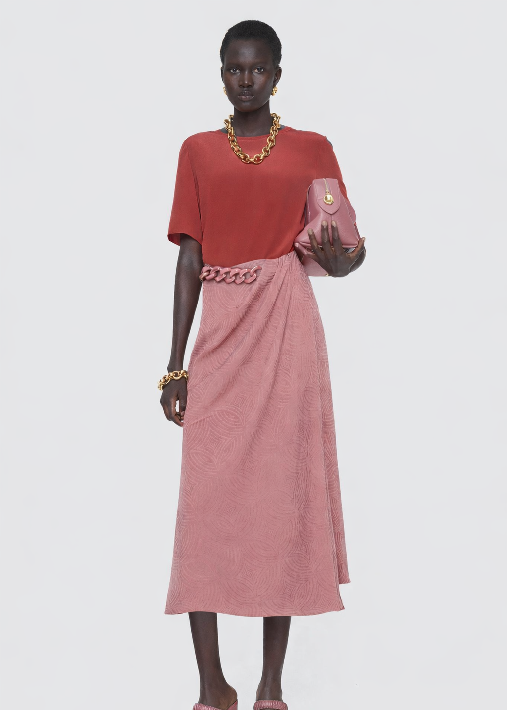 Woman wearing a red top and pink skirt with gold jewelry on a white background