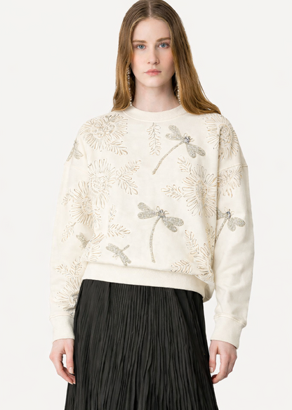 Woman wearing a cream sweater with floral patterns on a white background