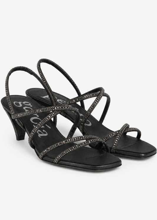 A pair of black strappy high-heeled sandals embellished with sparkling rhinestones, shown against a plain light gray background.