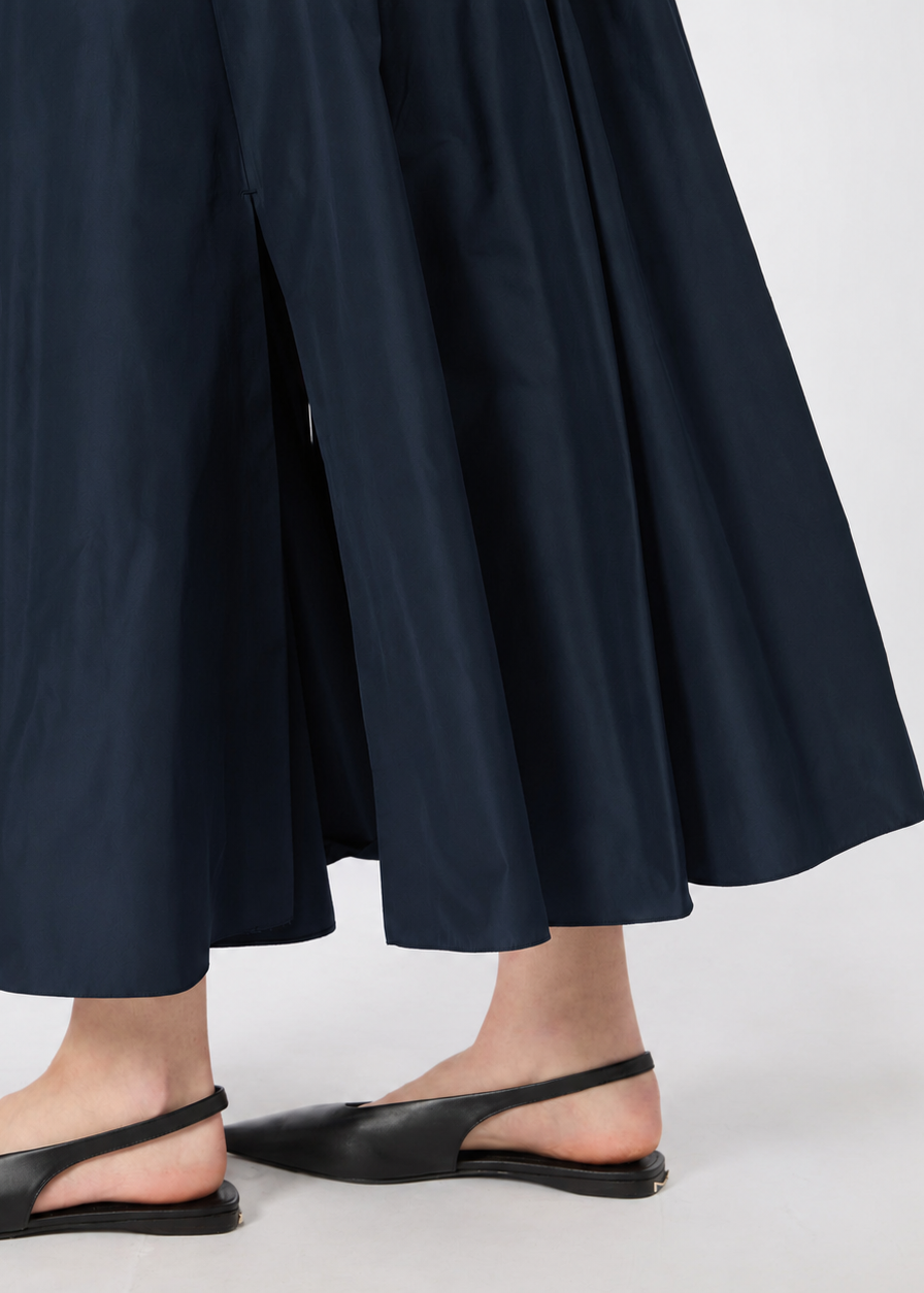 A close-up of a person wearing dark navy wide-leg cropped pants and black pointed slingback flats against a light gray studio background.