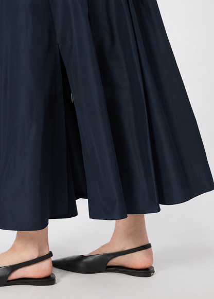 A close-up of a person wearing dark navy wide-leg cropped pants and black pointed slingback flats against a light gray studio background.