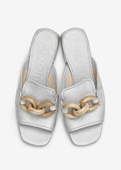 Pair of silver sandals with wooden chain details on a white background