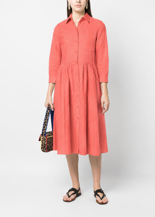 Woman wearing a coral dress holding a patterned bag on a white background