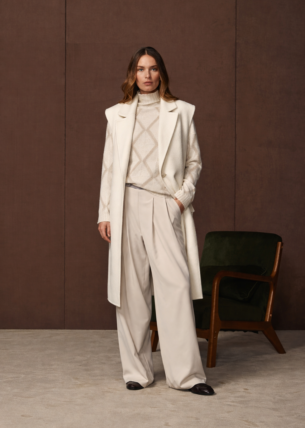 Woman wearing a beige coat and pants standing against a brown wall.