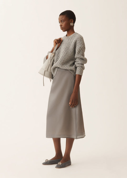 Woman wearing a patterned sweater and satin skirt on a plain background