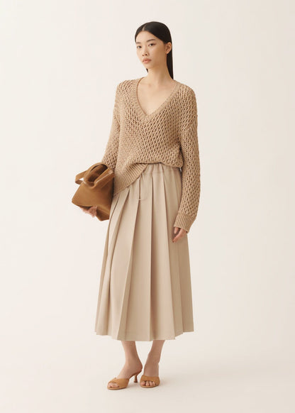 Woman wearing a beige knit sweater and skirt holding a brown bag on a white background